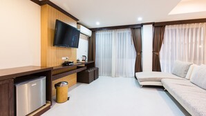 A modern living room with a flat-screen TV mounted on the wall, a sofa, a small coffee table, a trash bin, and a mini-fridge. - The Nine Hotel at Ao Nang (Krabi)
