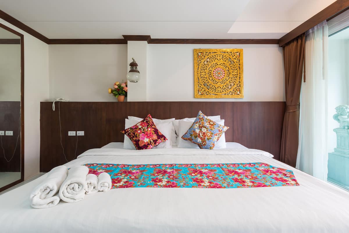 Camera d'albergo con un letto grande, due cuscini decorativi, una coperta colorata e vista su un balcone.