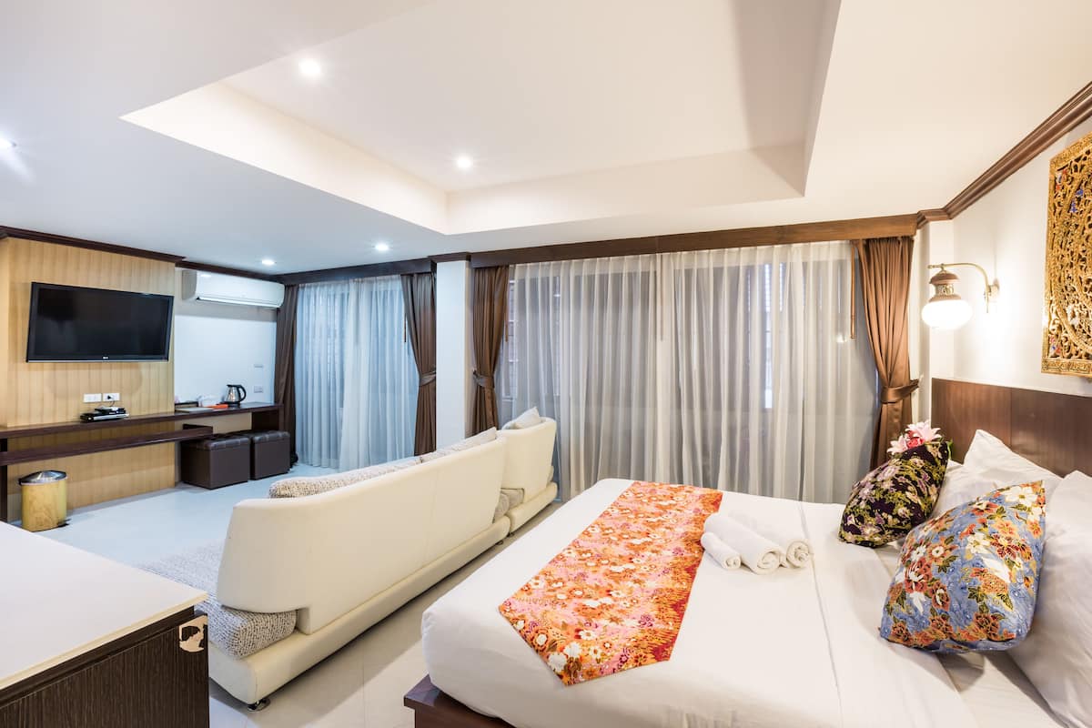 Una camera d'albergo moderna con un divano, un letto con biancheria a fiori, una TV e un angolo scrivania.