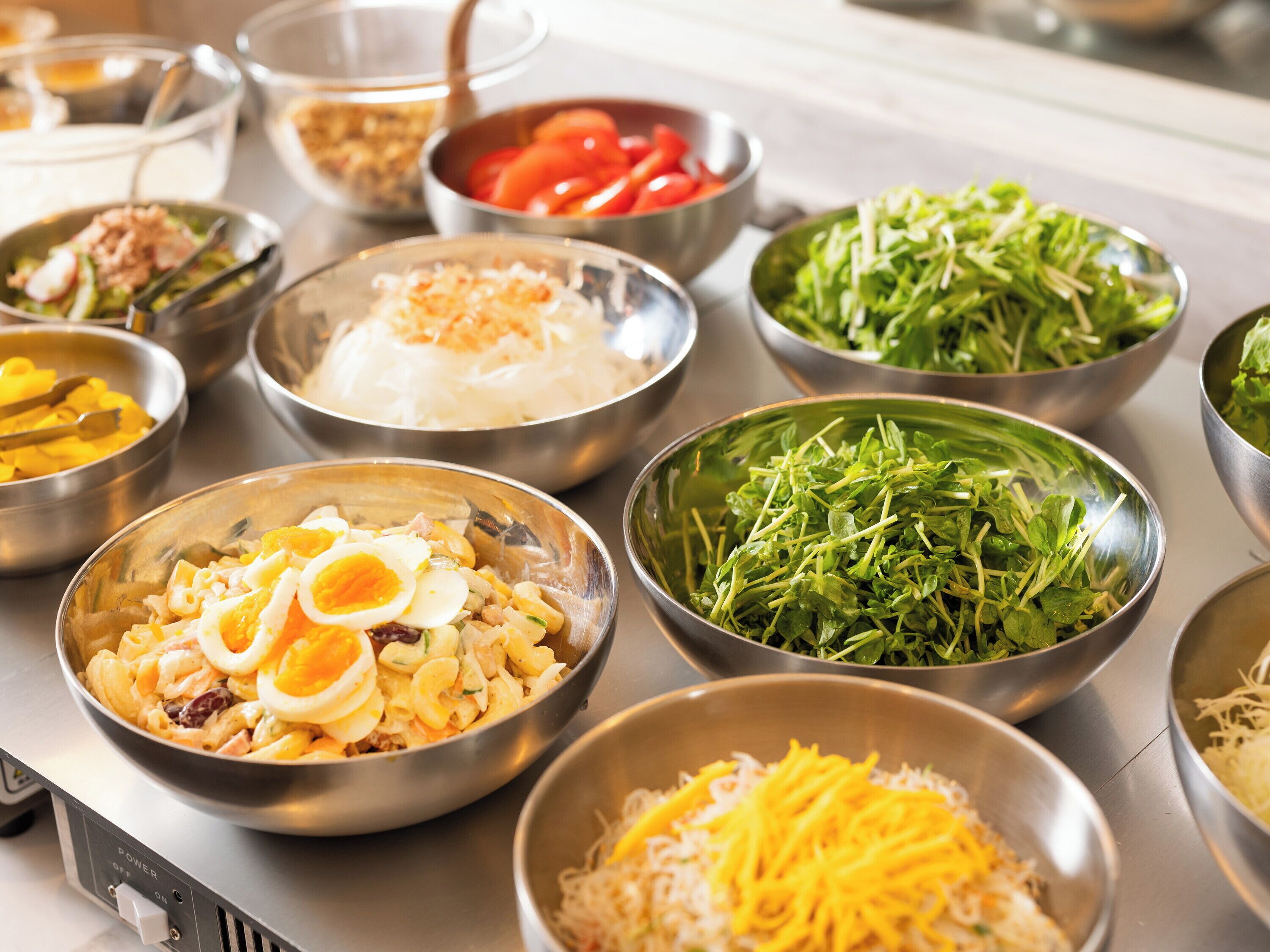 A buffet with various dishes in metal bowls, including pasta, salad, and rice.
