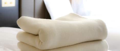 Una manta beige bien doblada sobre una cama con un almohadón blanco y un cabecero al fondo.