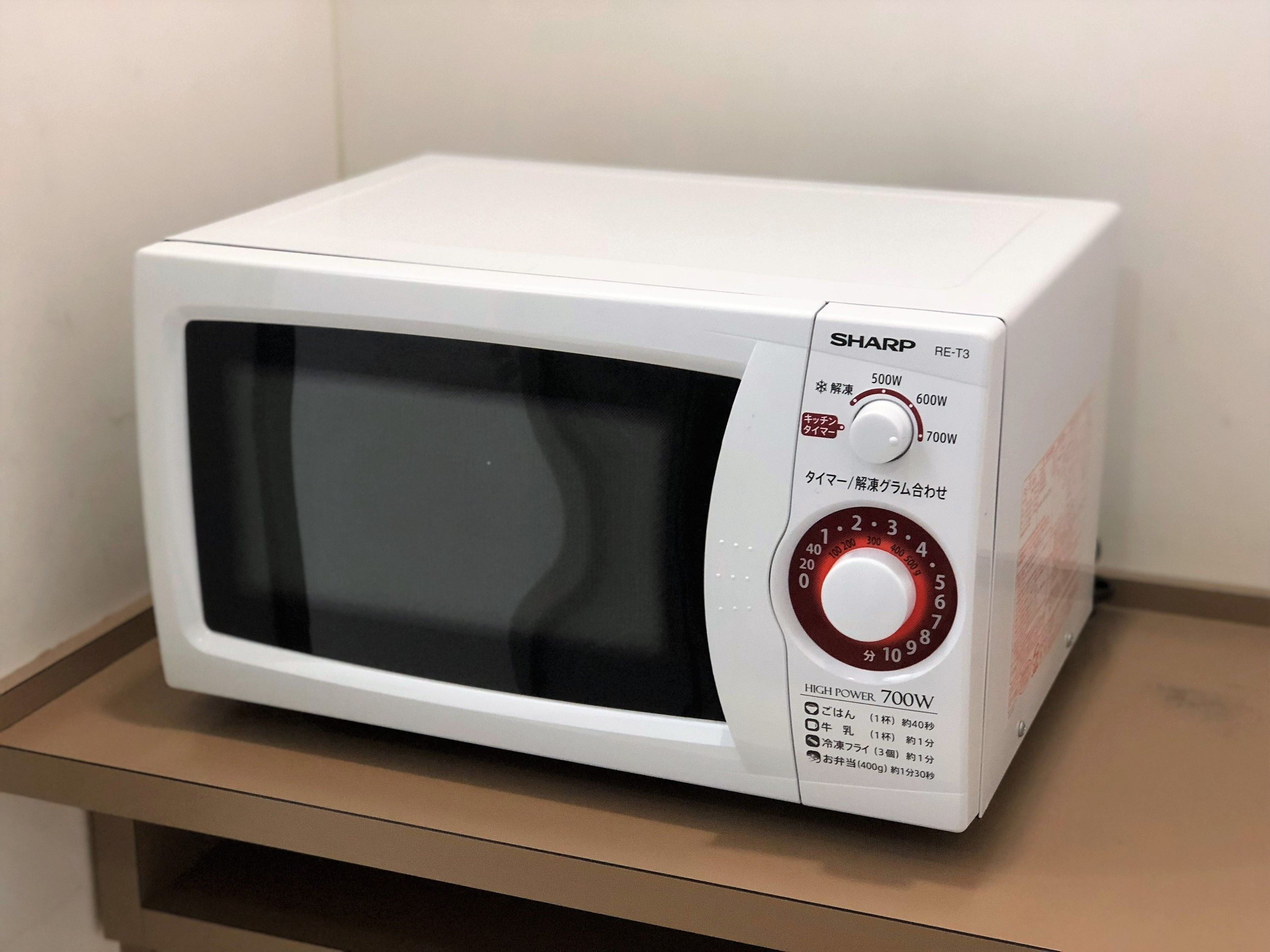 A white Sharp microwave oven with a digital display and a red dial, placed on a wooden shelf.