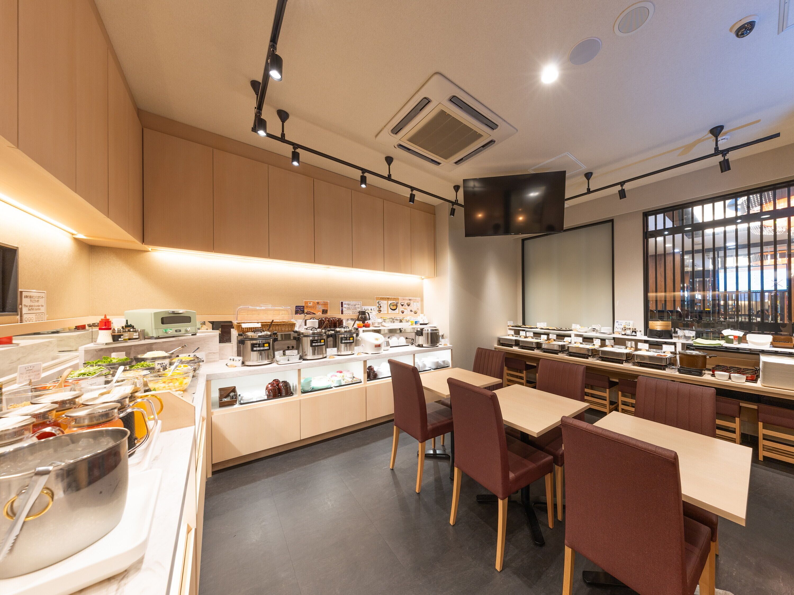 Un café moderno con barra de desayuno tipo buffet, zona de estar y una gran pantalla de televisión.