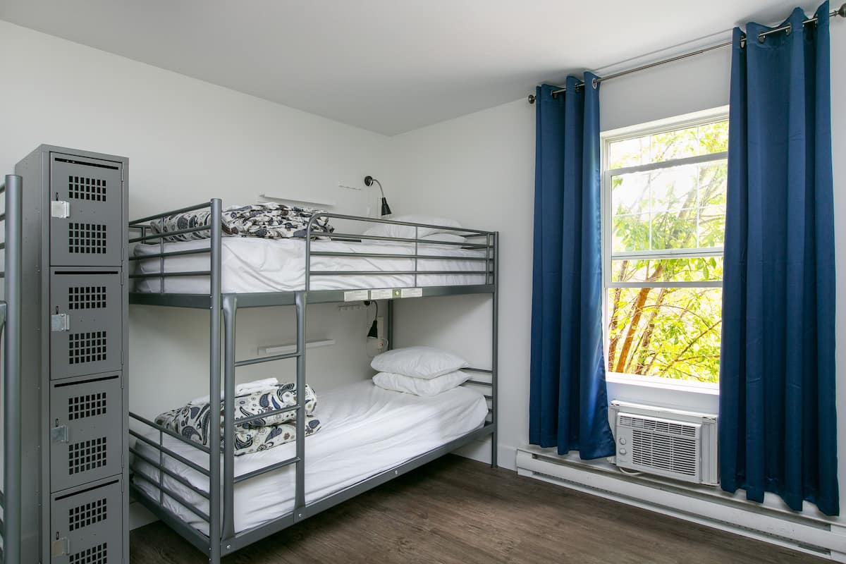 Habitación con literas, ventana, aire acondicionado y armario metálico.