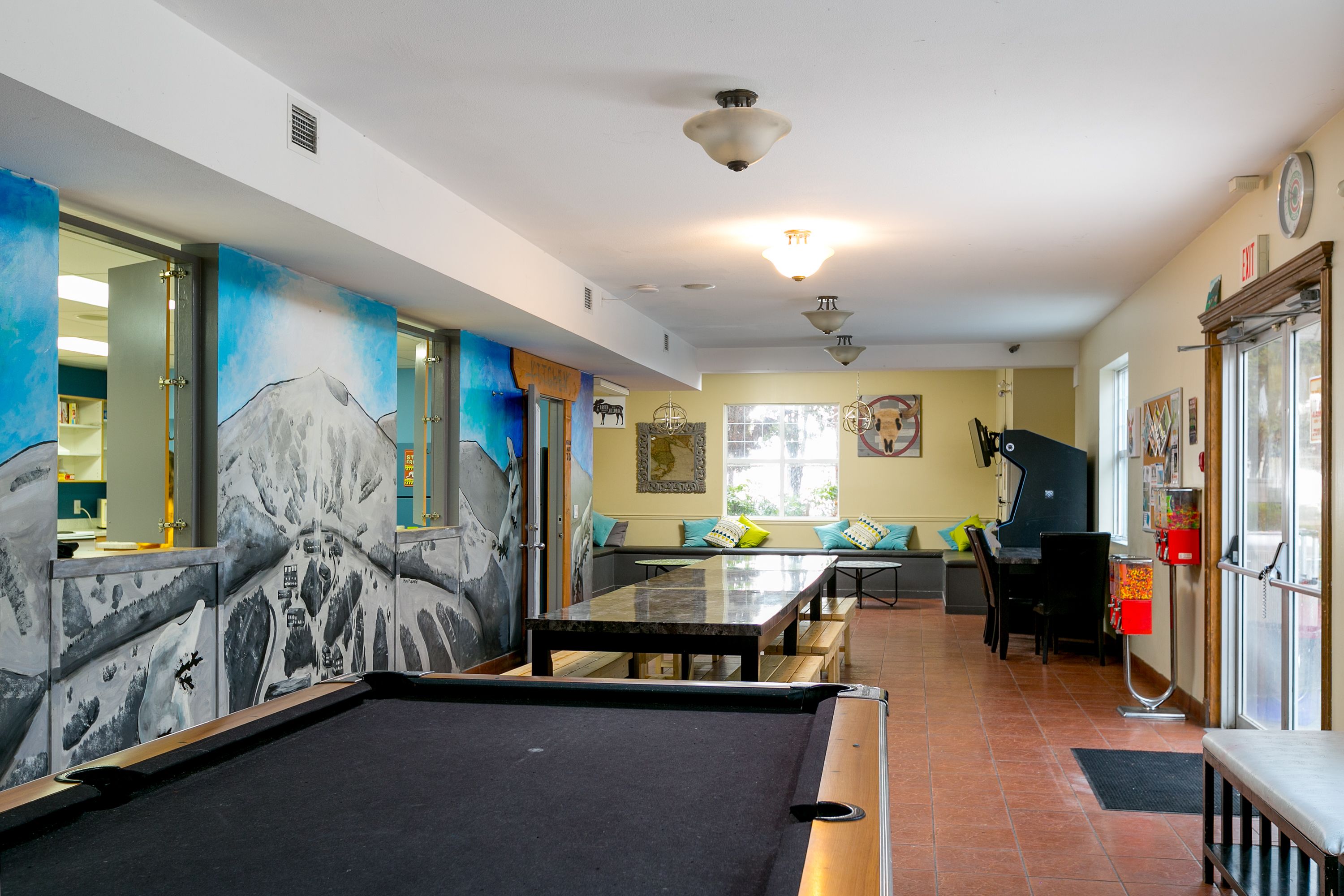 A pool table in a room with a mural, a piano, and a dining area with benches.