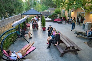 An outdoor patio area with seating arrangements including a swing chair, a bench, and a picnic table. There are potted plants and a covered seating area. -  HI Kelowna Hostel (Kelowna)