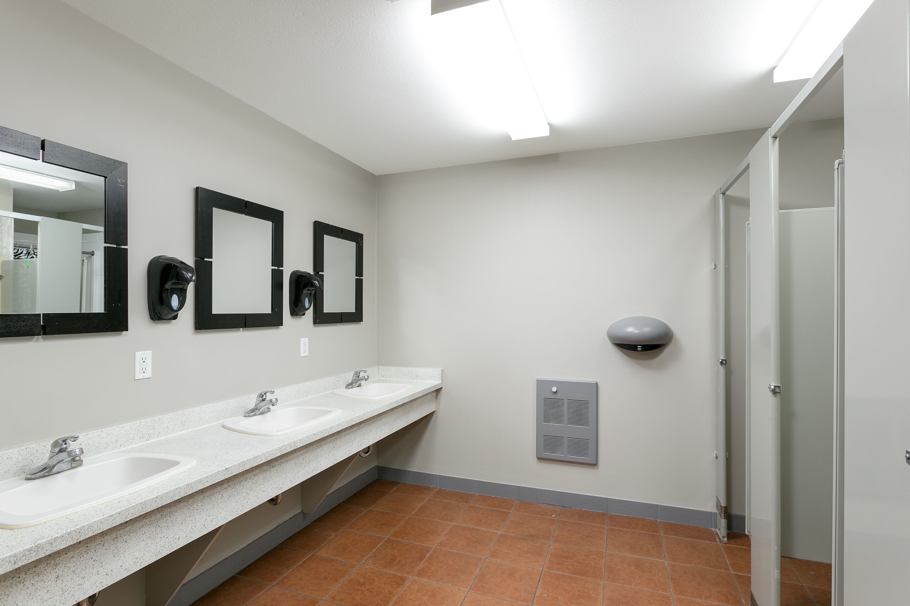 A clean, modern bathroom with two sinks, three mirrors, a hand dryer, and a ventilation unit.