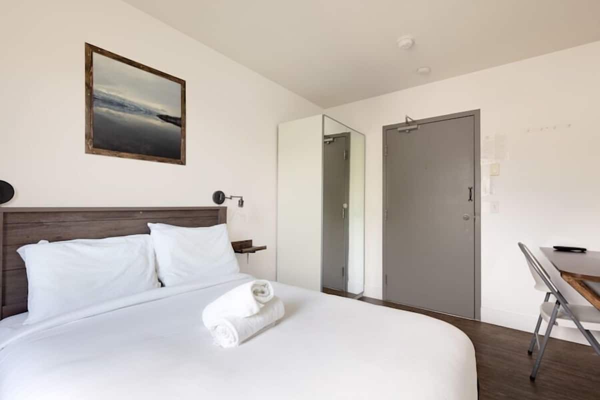 Una habitación de hotel con una cama grande, una mesita de noche, un escritorio y un armario.