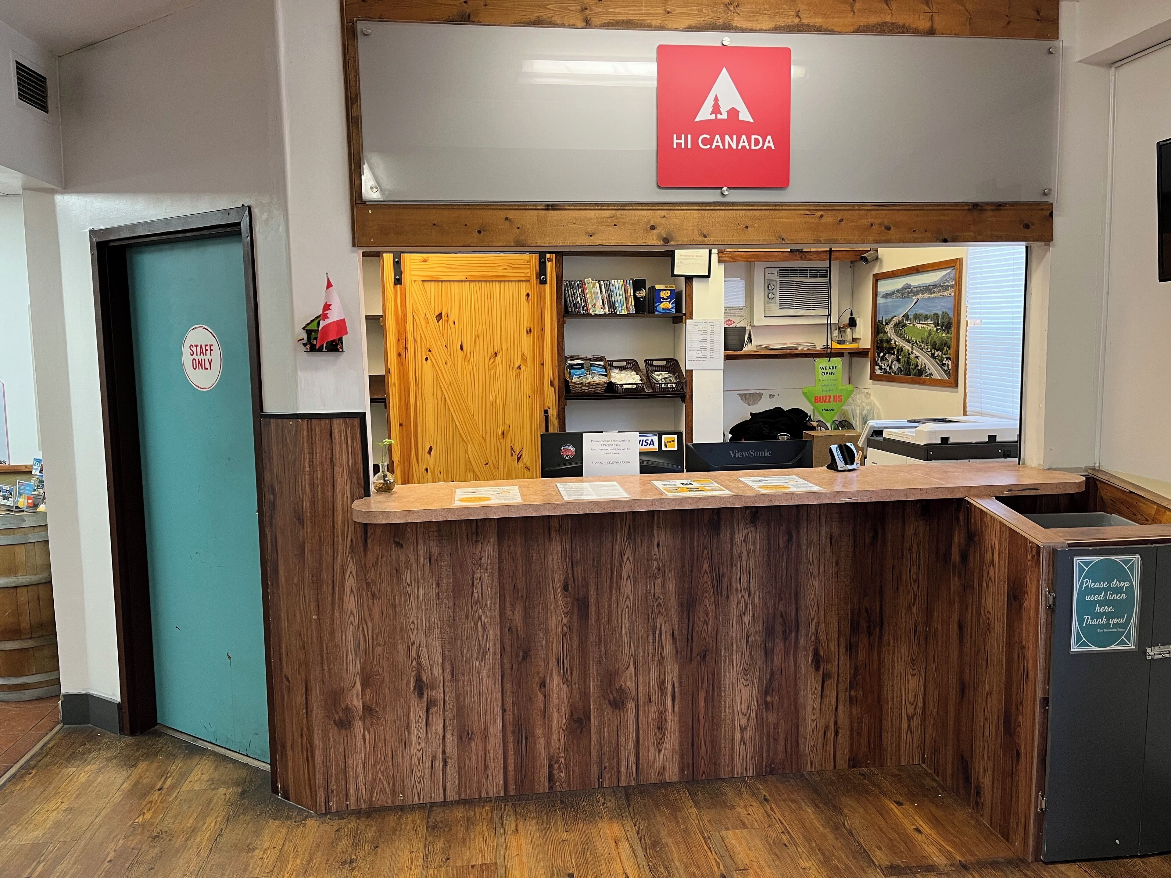 A reception desk with a 'Staff Only' sign, a 'HI CANADA' sign above, and a 'Please drop used linen here. Thank you.' sign on the right.