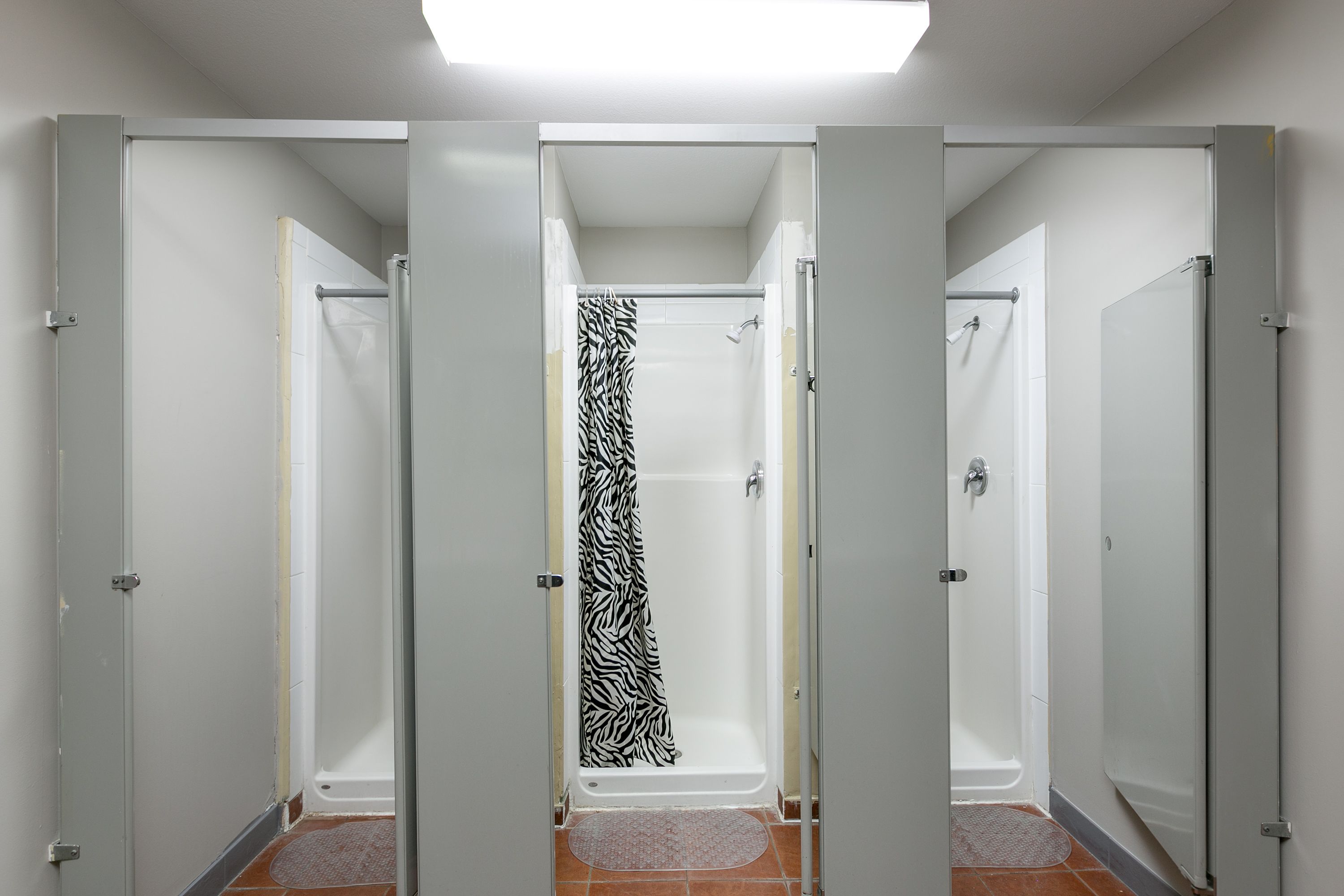 Une salle de bain avec trois cabines de douche, chacune équipée d’un rideau de douche blanc et d’un porte-serviettes.