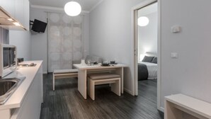 Une chambre d’hôtel compacte comprenant un coin cuisine, une petite table à manger, un lit et un miroir.