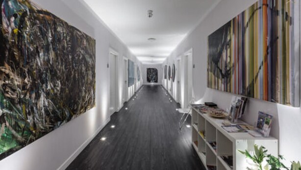 Un couloir doté d’un long plancher en bois sombre, de murs blancs et de grandes peintures abstraites de part et d’autre.