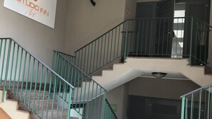 Un escalier avec des rampes vertes mène à l’étage supérieur. Une enseigne sur le mur indique : « STUDIO INN Art ».