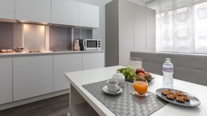Une cuisine moderne avec des meubles blancs, un four à micro-ondes et un coin petit-déjeuner comprenant une théière, une tasse et des fruits.