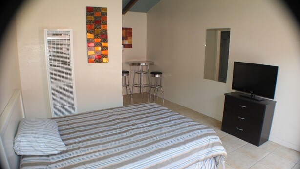 A bedroom with a bed, a TV, a dresser, and a small bar area with stools. - International Casa (Oakland)