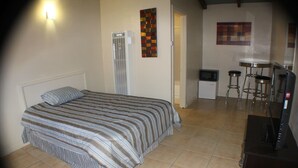 A bedroom with a bed, a heater, a small kitchenette, and a bar area. - International Casa (Oakland)