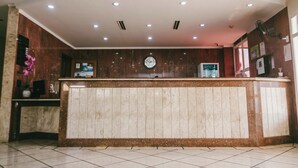 A reception area with a marble counter, a clock, and a fan on the wall. - Hotel Almanara (Cuiabá)