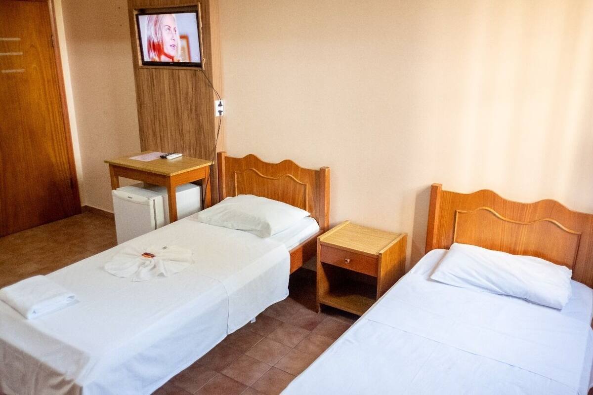 Una habitación de hotel con dos camas individuales, un cabecero de madera, una pequeña mesa de madera, un televisor montado en la pared y un escritorio con una silla.