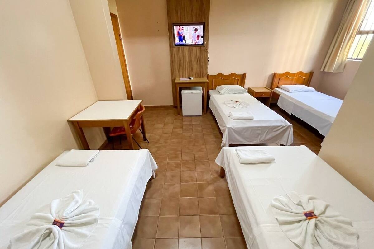 Una habitación de hotel con cuatro camas individuales, un televisor montado en la pared, una mesita pequeña y un escritorio.