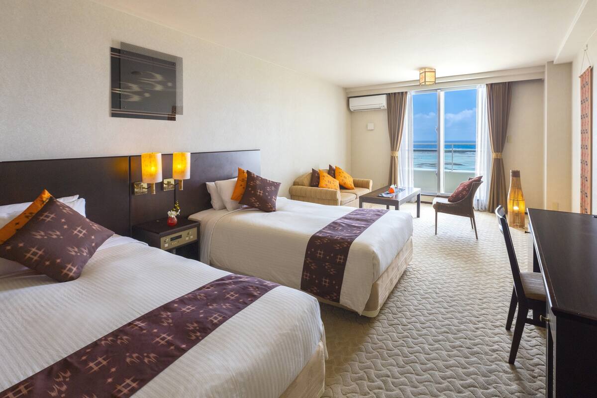 Ett hotellrum med två sängar, ett skrivbord, en stol och utsikt över havet.