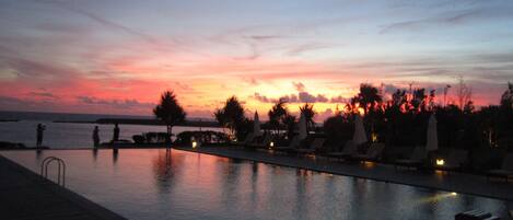 Zona junto a la piscina con sillones reclinables y sombrillas, con vista a un cuerpo de agua durante el atardecer.