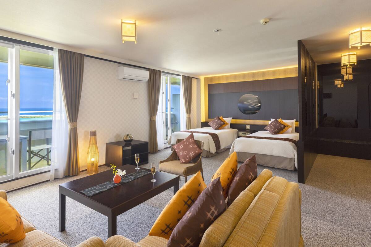 Ett hotellrum med en soffa, två sängar, ett soffbord och utsikt över havet.