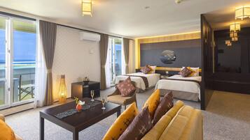 A hotel room with a sofa, two beds, a coffee table, and a view of the ocean.