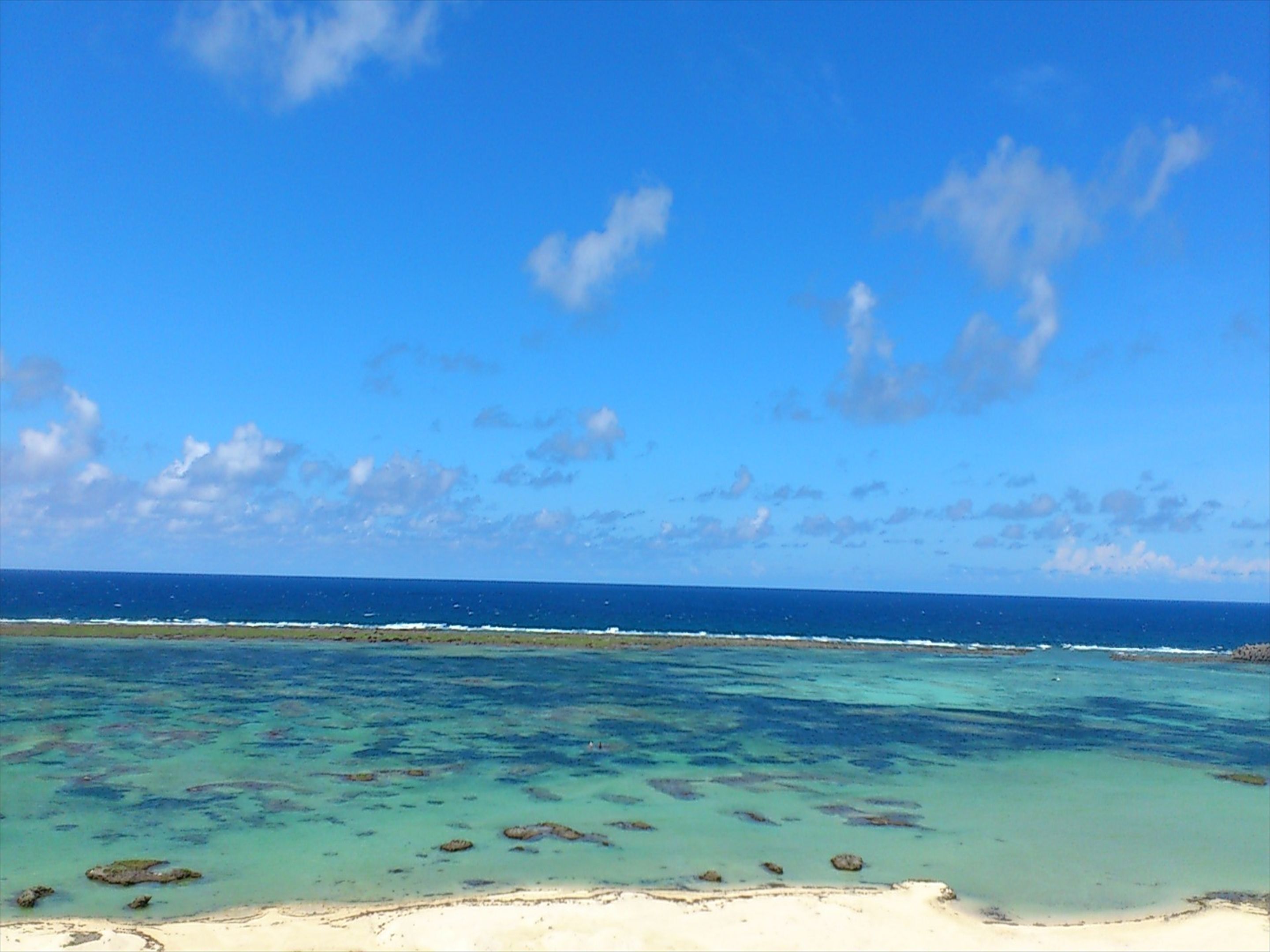 A beach with clear turquoise water, a sandy shore, and a distant horizon.