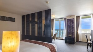 A hotel room with a large bed, a desk, a chair, a balcony with a view, and a decorative wall panel. - Cypress Resort Kumejima (Kumejima)