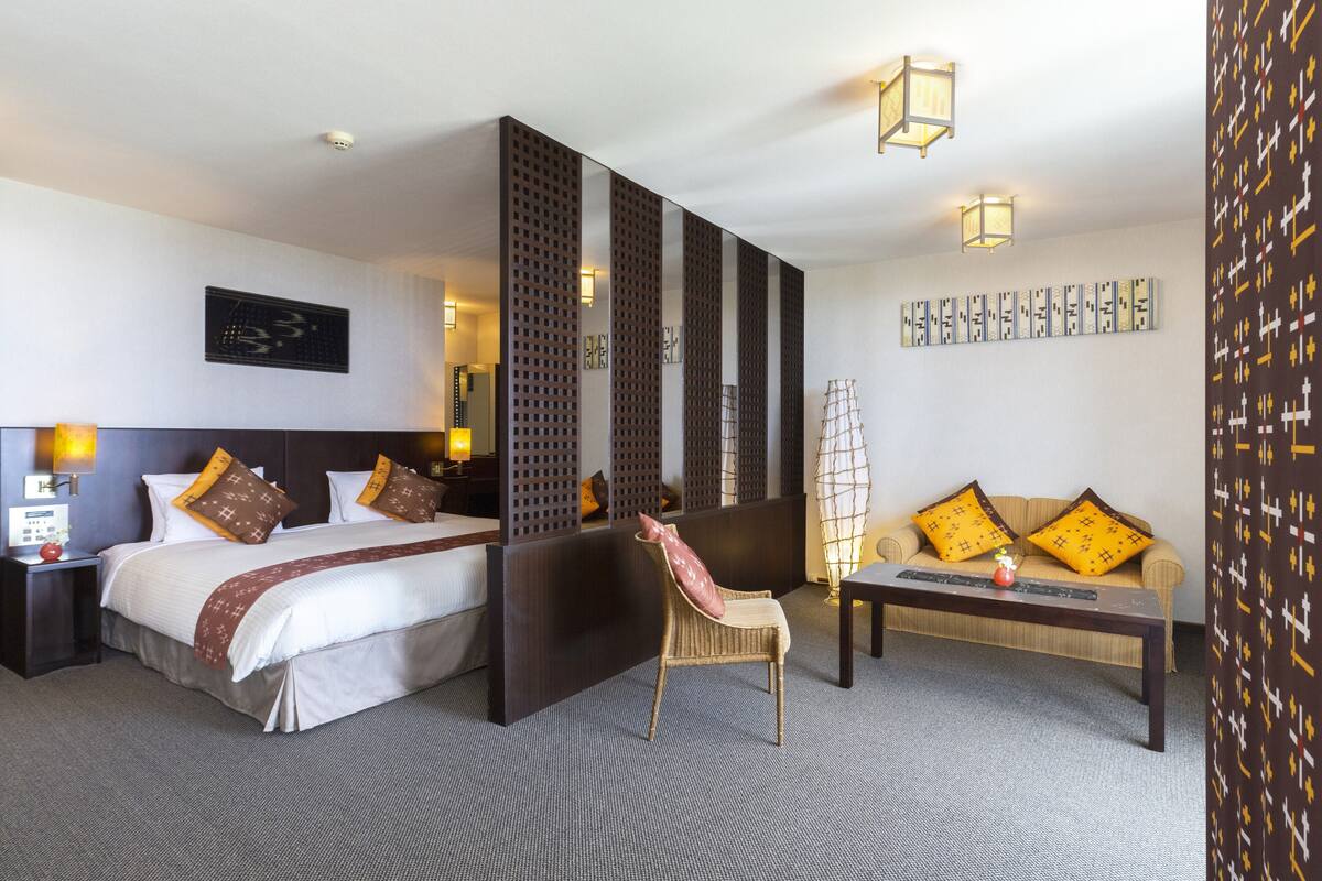 Ett hotellrum med en säng, en soffa, en fåtölj, ett soffbord och en dekorativ skärm.