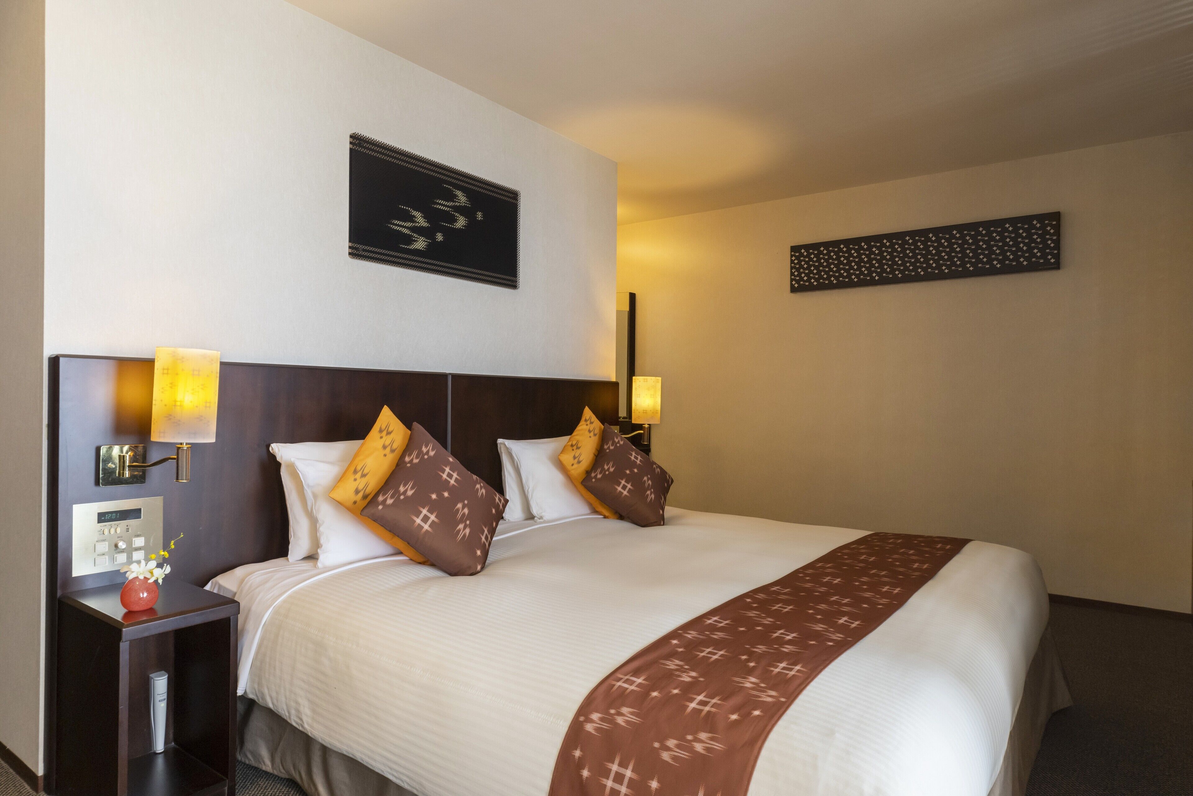 A hotel room with a large bed, two bedside lamps, a nightstand with a vase of flowers, and a wall clock.