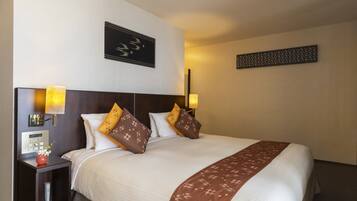 A hotel room with a large bed, two bedside lamps, a nightstand with a vase of flowers, and a wall clock.
