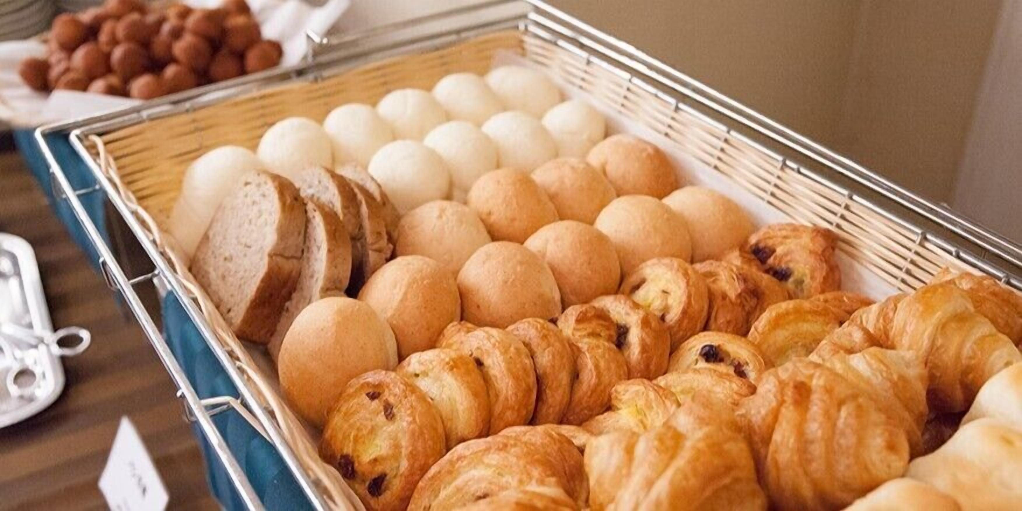 A display of various baked goods including bread, croissants, and round pastries, likely in a bakery or cafe setting.