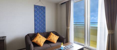 A room with a sofa, a coffee table, and a view of the sea through large windows.