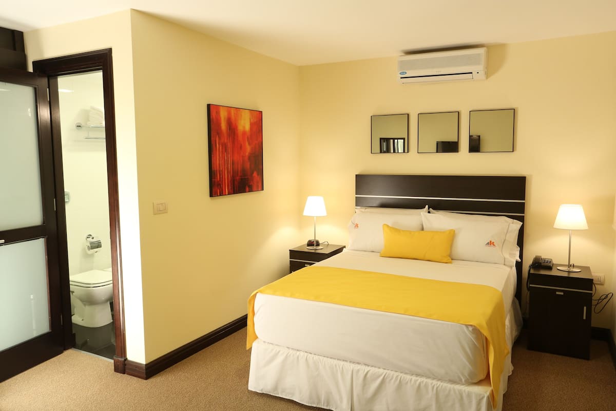 Ein Hotelzimmer mit einem Bett, zwei Nachttischen, einem Spiegel und einer Klimaanlage.