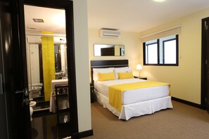 Habitación de hotel con cama, mesita de noche, lámpara, aire acondicionado y ventana con persianas.