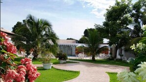 A garden pathway leading to a building with a tiled roof, surrounded by lush greenery and potted plants. - Delcas Hotel (Cuiabá)