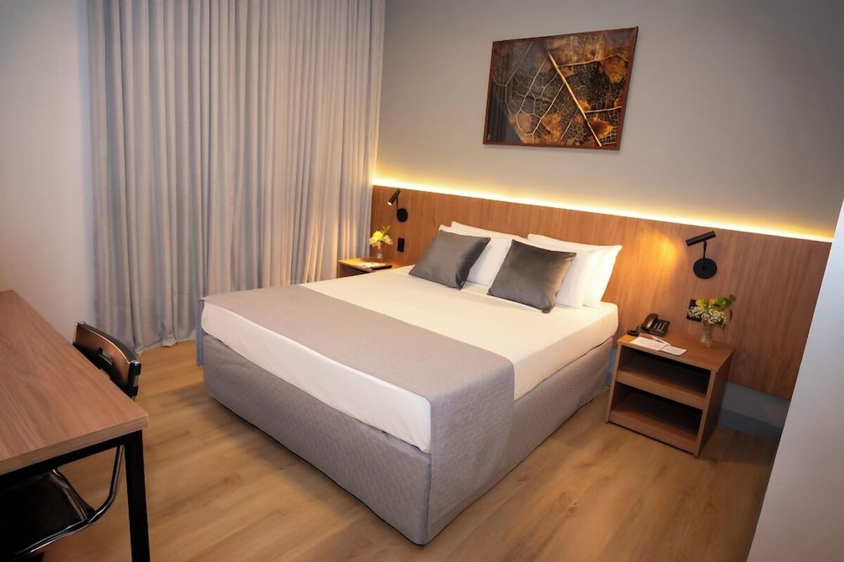 A modern hotel room with a large bed, bedside tables, a desk, and a wall-mounted artwork.
