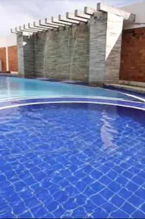 Ein Schwimmbad mit Fliesenboden und einer Steinmauer mit Metallgeländer.