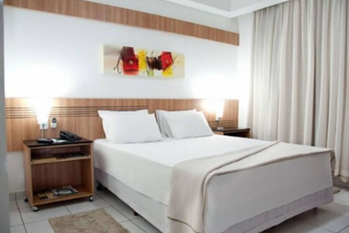 Una habitación de hotel con una cama, mesitas de noche, un escritorio y una obra de arte colgada en la pared.