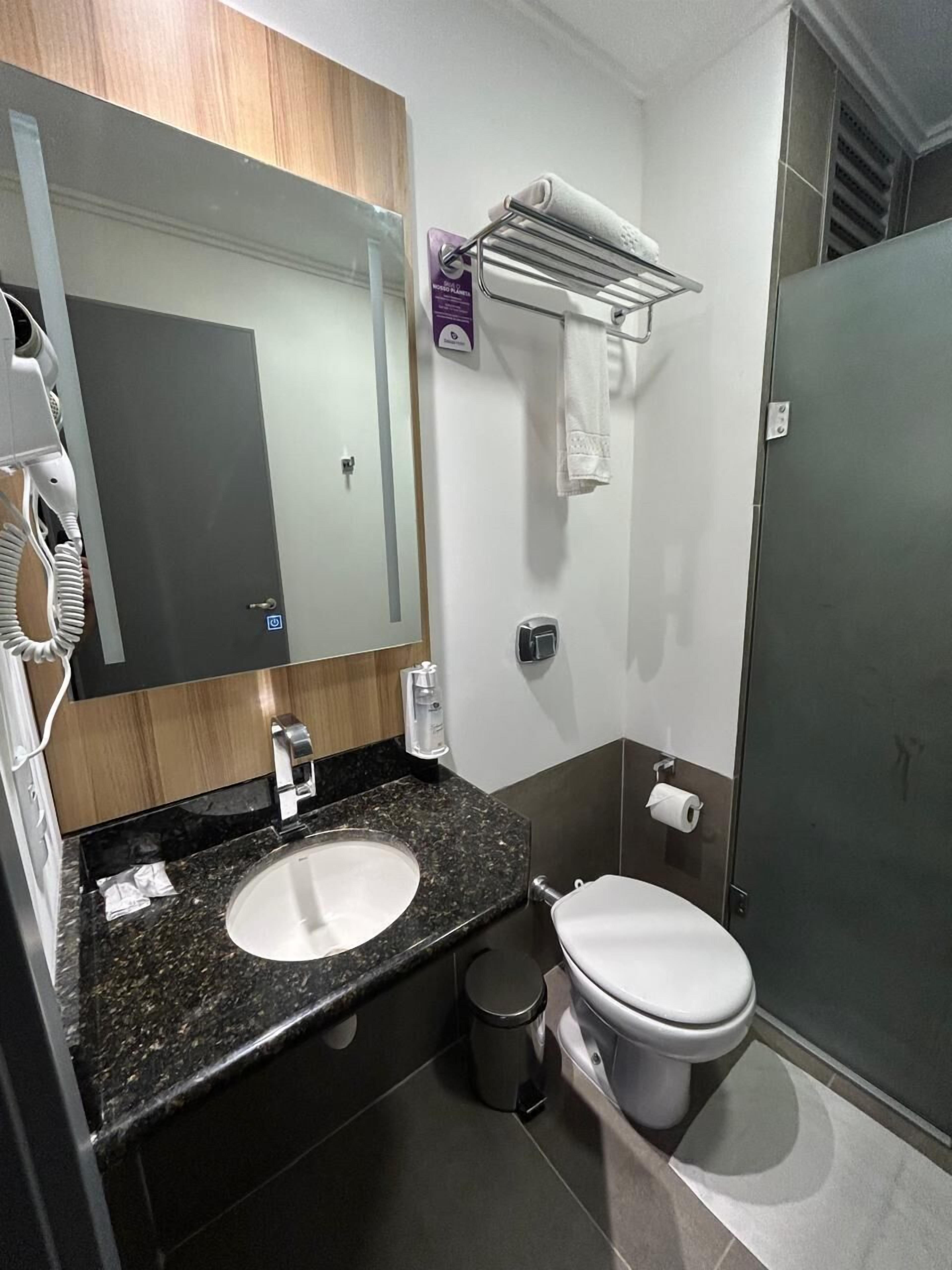 A modern bathroom with a granite countertop sink, a toilet, a hand dryer, and a towel rack.