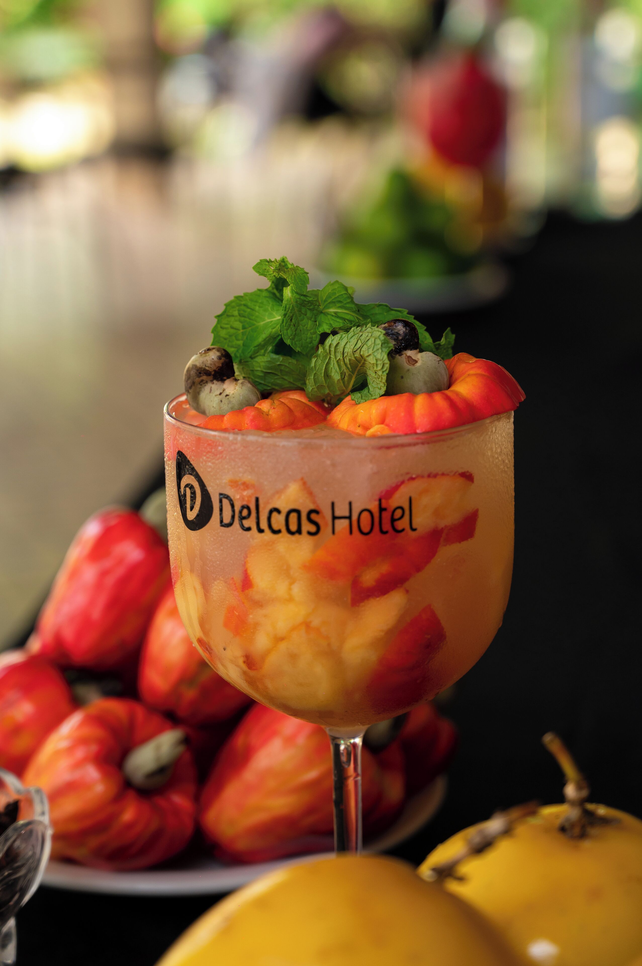 Un verre à cocktail décoré de fruits et de feuilles de menthe, avec l’inscription « Hôtel Delcas ».