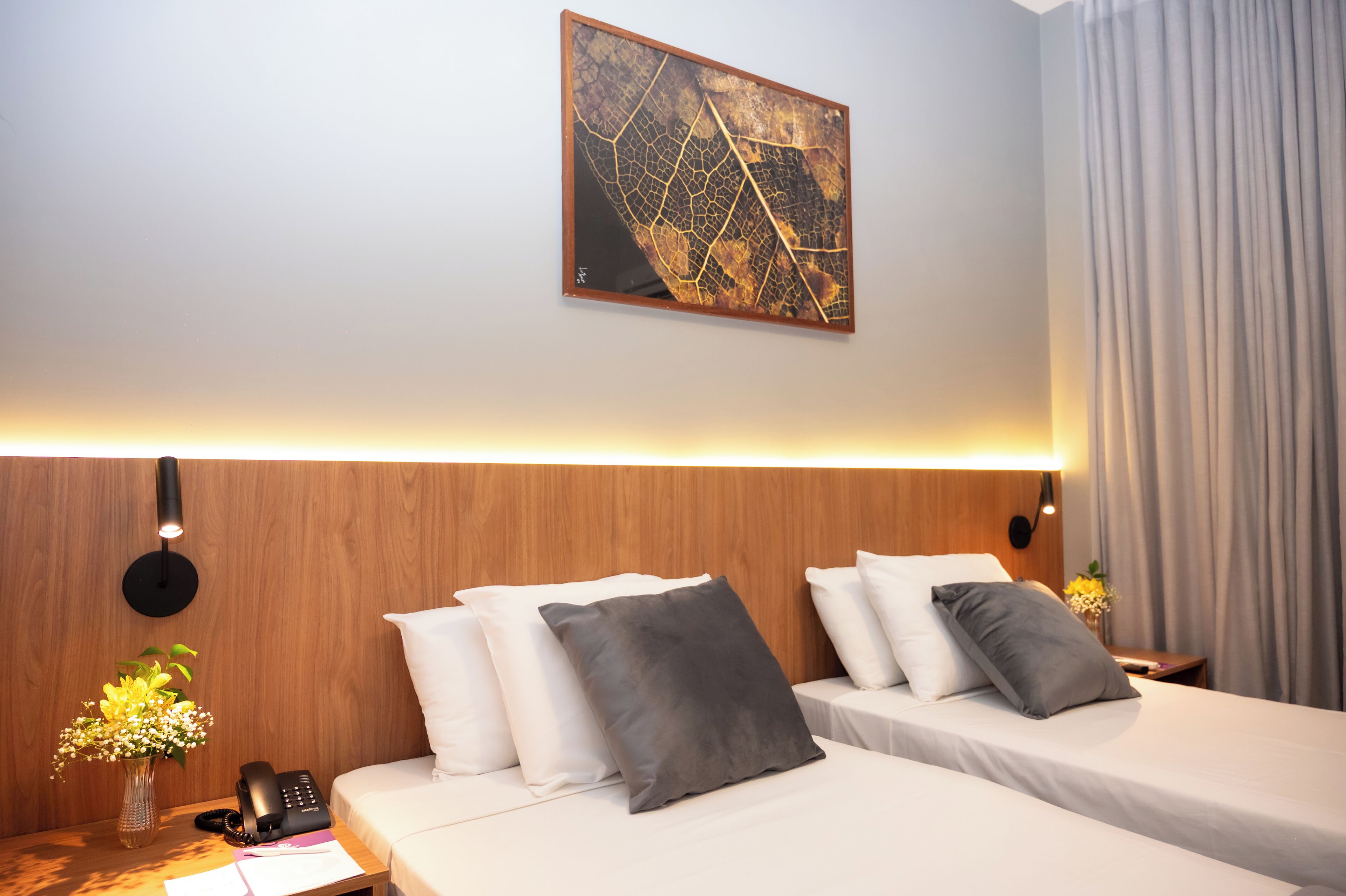 Habitación de hotel con dos camas, cabecero de madera, una obra de arte colgada en la pared, mesita de noche con un teléfono y un jarrón de flores.