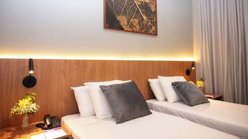 Habitación de hotel con dos camas, cabecero de madera, una obra de arte colgada en la pared, mesita de noche con un teléfono y un jarrón de flores.