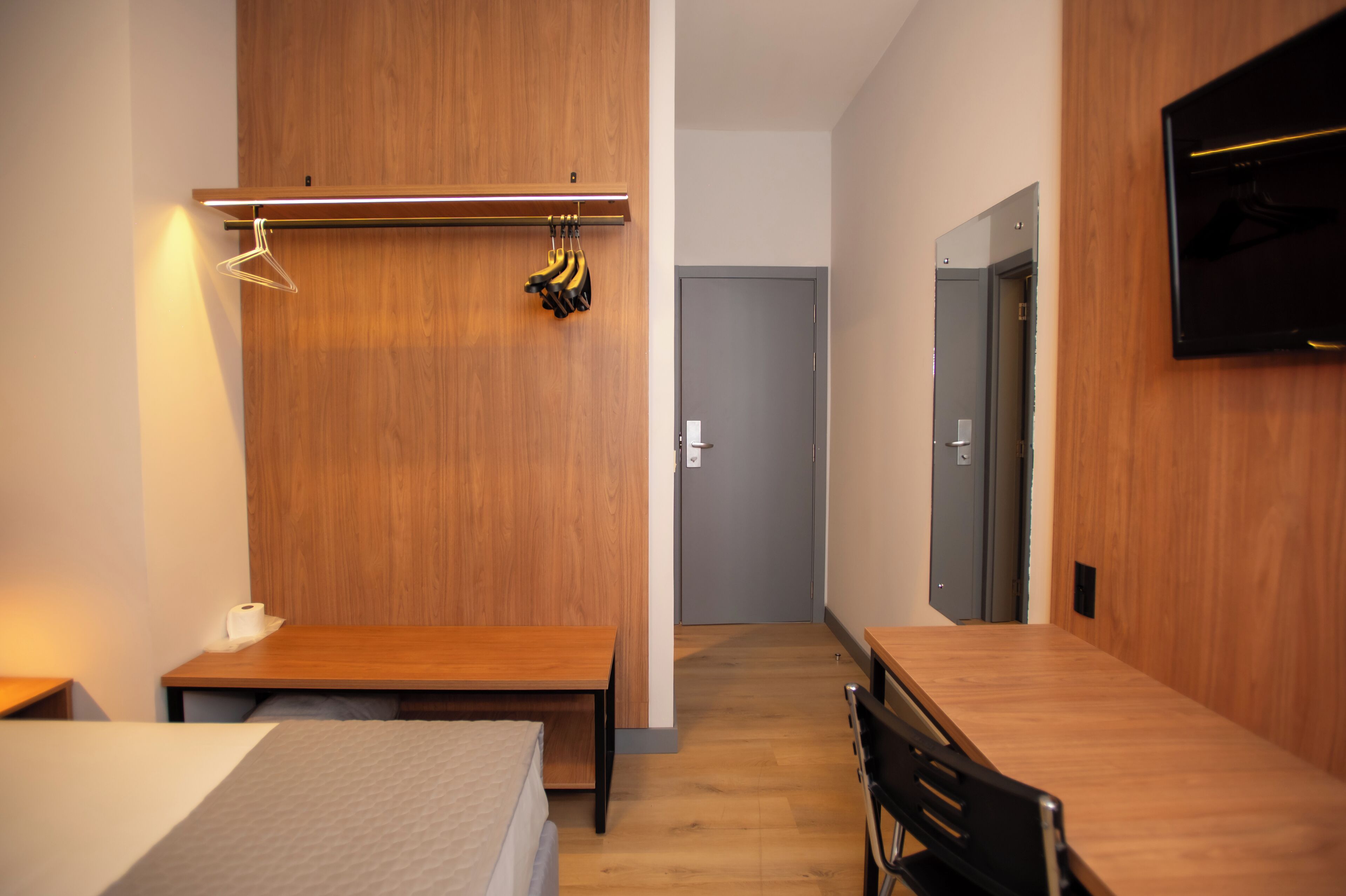 A modern hotel room with a wooden floor, a bed, a desk, and a TV mounted on the wall.