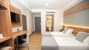 A hotel room with two beds, a desk, a chair, a TV, and a bathroom visible through an open door. - Delcas Hotel (Cuiabá)