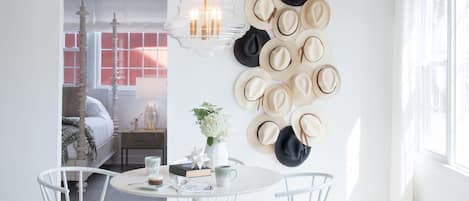 A bright dining area with a round table, white chairs, and a wall-mounted hat collection.