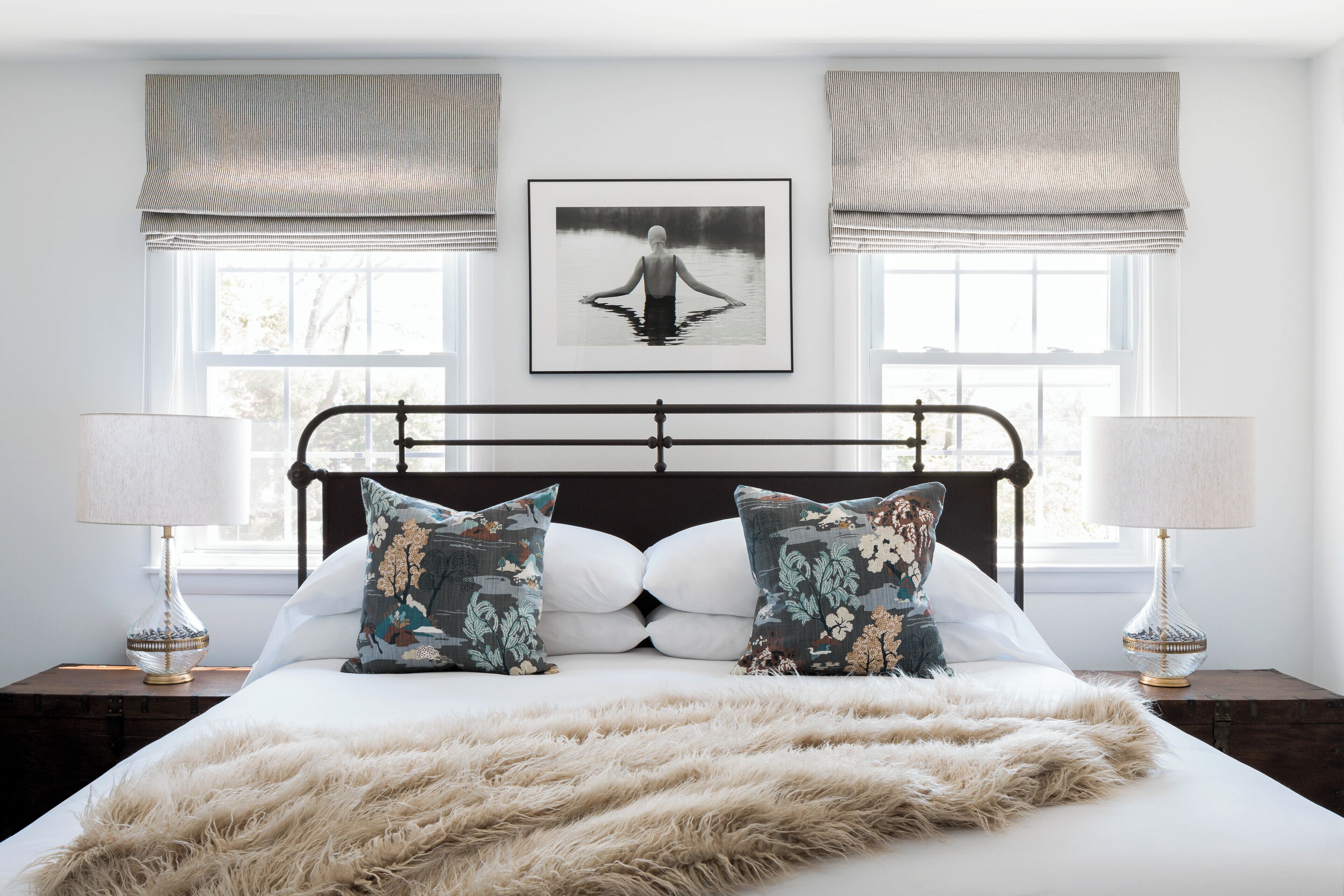 A bedroom with a large bed, two bedside lamps, a framed picture on the wall, and a window with curtains.