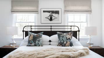A bedroom with a large bed, two bedside lamps, a framed picture on the wall, and a window with curtains.