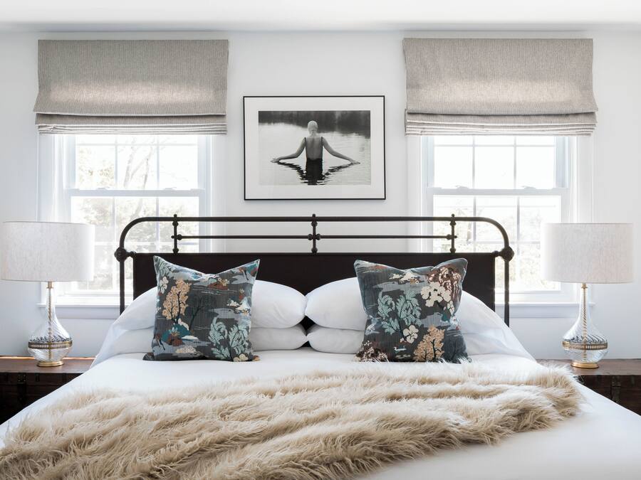 Un dormitorio con una cama grande, dos lámparas de noche, un cuadro enmarcado en la pared y una ventana con cortinas.